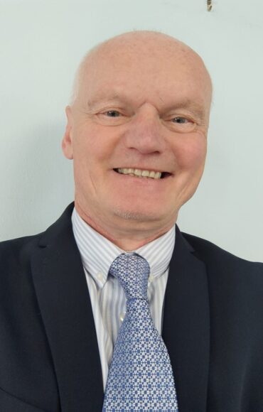 A man in a suit and tie smiles warmly, exuding confidence and professionalism.