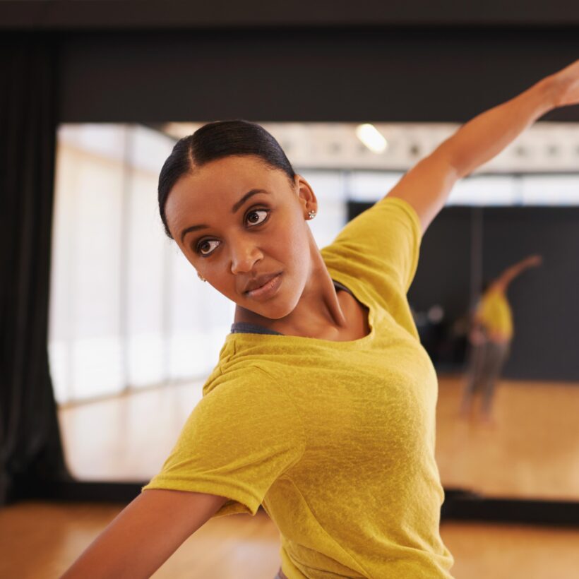 A woman in a vibrant yellow shirt engages in a dynamic dance, embodying joy and movement.