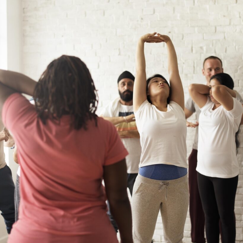 A diverse group of individuals stands in a room, stretching before their class