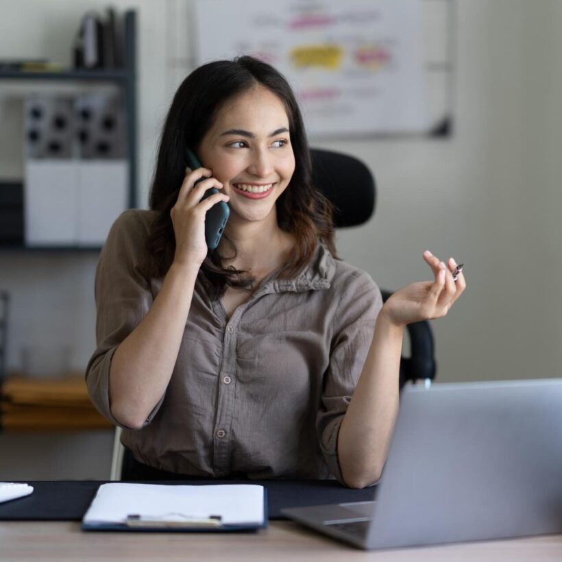 A woman talking on the phone while sitting at her desk, showcasing a moment of communication in a work environment.